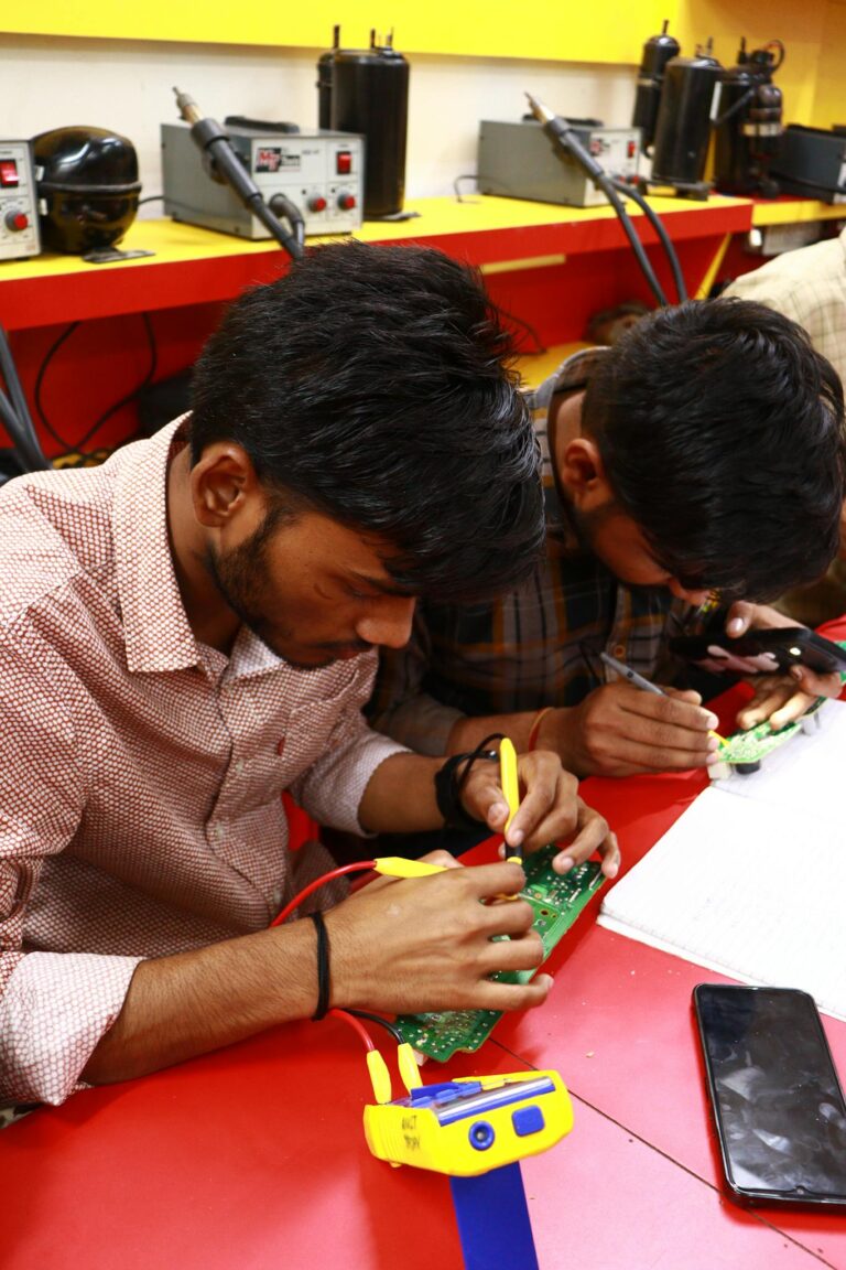 Young men learning PCB repair technique in electronic workshop.